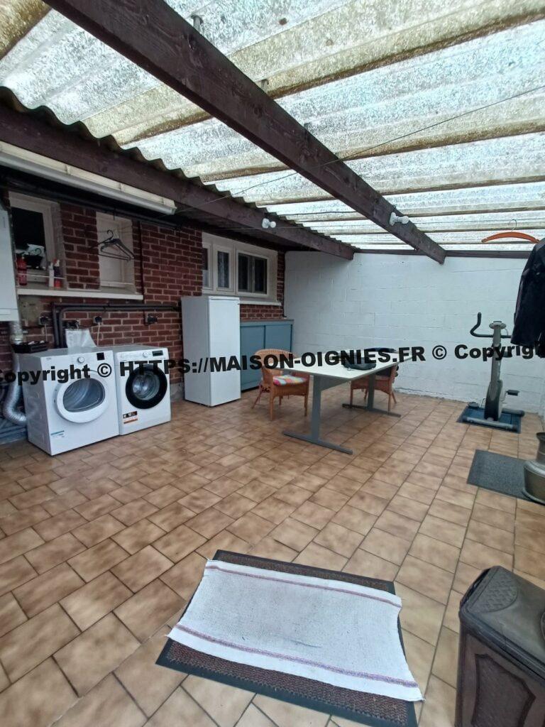 L'image montre la buanderie depuis la porte qui donne sur l'allée du jardin, une chaudière Wiessmann parfaitement entretenue est installée sur la gauche, sèche-linge, machine à laver, un congélateur et une armoire de rangement suivent vers la droite, une table y est installée pour l'hivernage des plantes ou autres utilisations