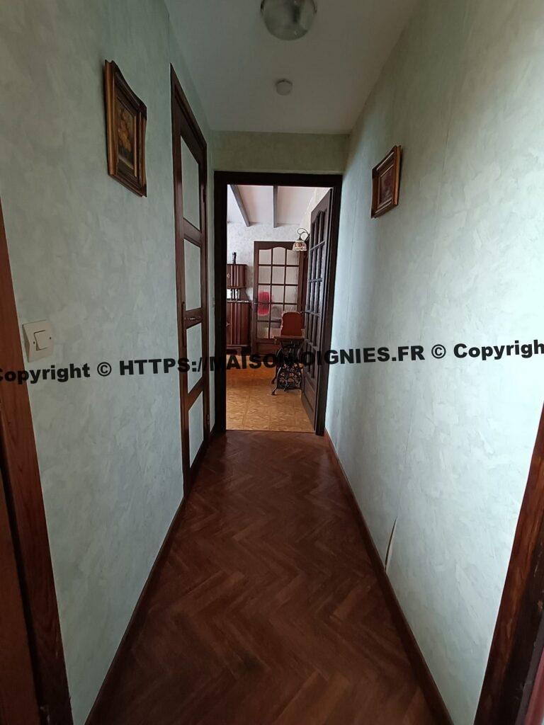 Vue du couloir depuis la porte d'entrée avec la vue sur la salle à manger, son revêtement synthétique qui imite un plancher, les murs sont tapissés en vert clair, les boiseries couleur noyer sont vernies