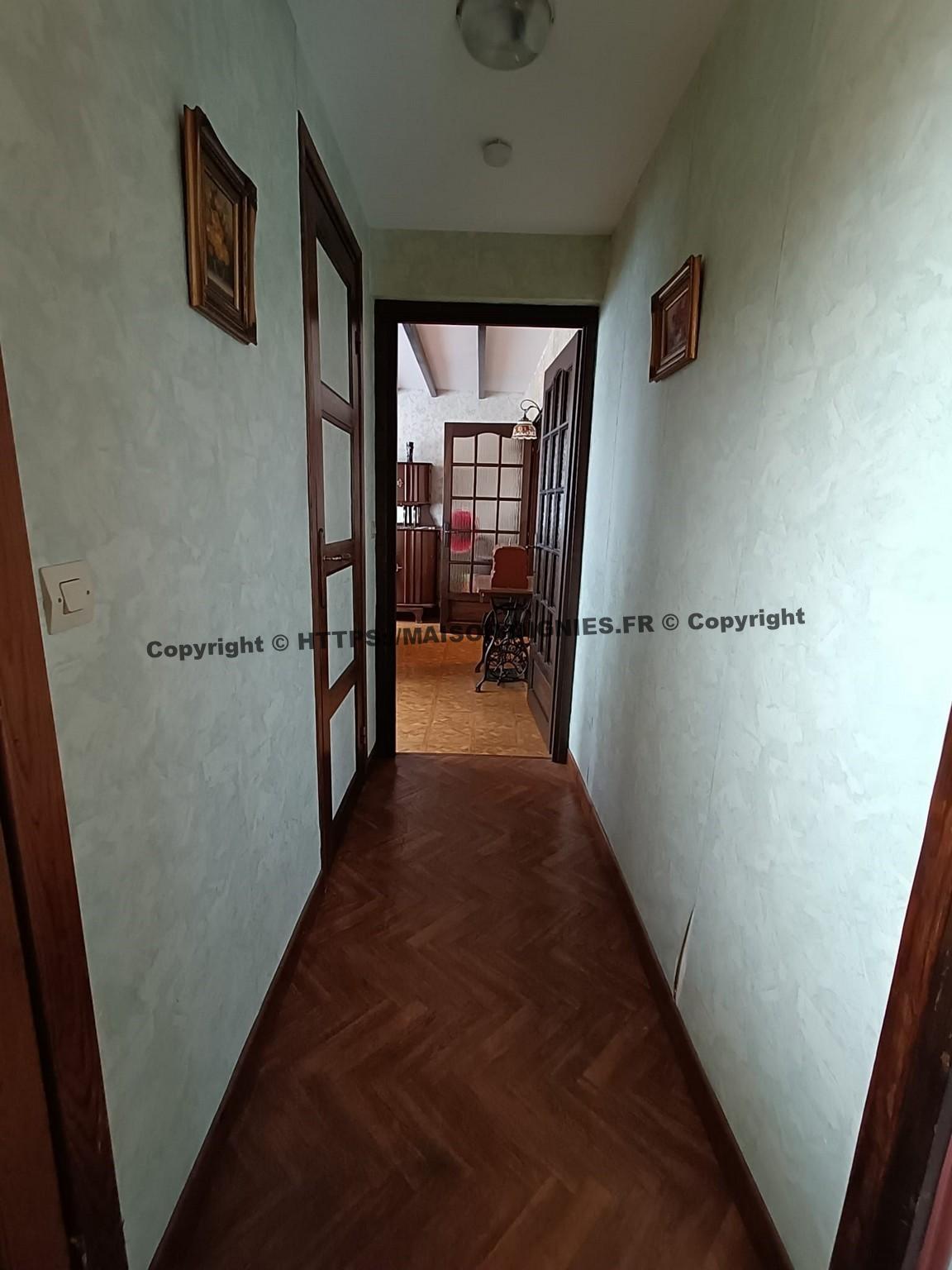 Vue du couloir depuis la porte d'entrée avec la vue sur la salle à manger, son revêtement synthétique qui imite un plancher, les murs sont tapissés en vert clair, les boiseries couleur noyer sont vernies