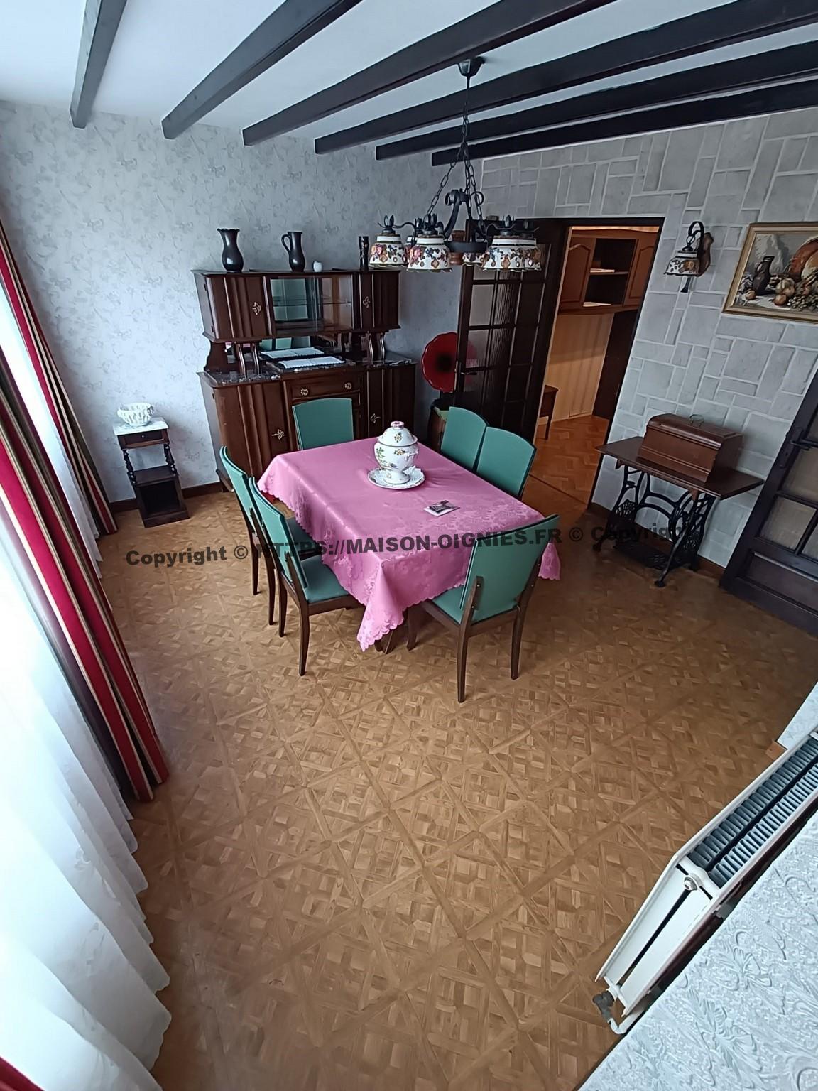 l'image en léger surplomb depuis le bas de l'escalier, montre la salle à manger actuelle, une table et six chaises vertes d'ancienne facture et un buffet vernis ancien, un lustre avec des caches céramiques, une machine à coudre ancienne sur le mur à droite et au fond un gramophone sur un petit tonneau en chêne de 50 litres